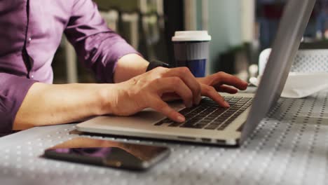 Mid-section-of-man-using-laptop-while-sitting-at-a-cafe