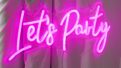 two female friends having fun in photo booth with neon "let's party" sign outside 1