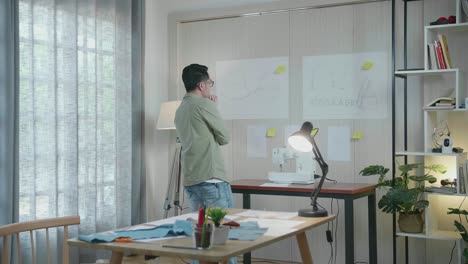 vista trasera del diseñador asiático mirando el papel de boceto de diseño en la pared