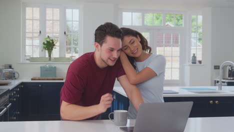 Loving-Transgender-Couple-At-Home-Together-Looking-At-Laptop-On-Kitchen-Counter