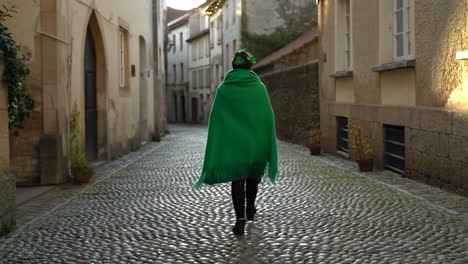 person in a green cloak walking on a cobblestone street with a shamrock hair accessory, symbolizing st. patrick's day