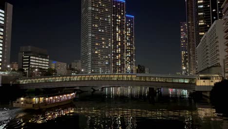 Paisaje-Urbano-Nocturno-Con-Edificios-Iluminados-Y-Un-Puente-Que-Se-Refleja-Sobre-El-Agua,-Escena-Urbana-Tranquila