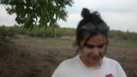 Mujer-Caminando-Por-Un-Campo-Rural-En-Un-Día-Nublado,-Sonriendo-Y-Disfrutando-De-La-Naturaleza.