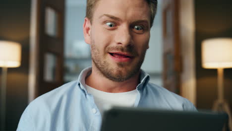 Excited-winner-rejoicing-tablet-at-room-zoom-on.-Closeup-guy-celebrating-success