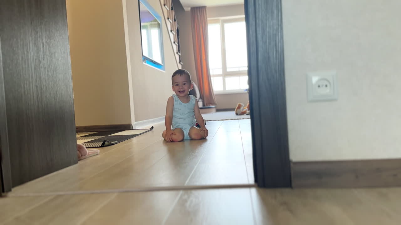 Happy crawling toddler laughs adorably to the camera. Sweet little kid moves by the floor in his house.