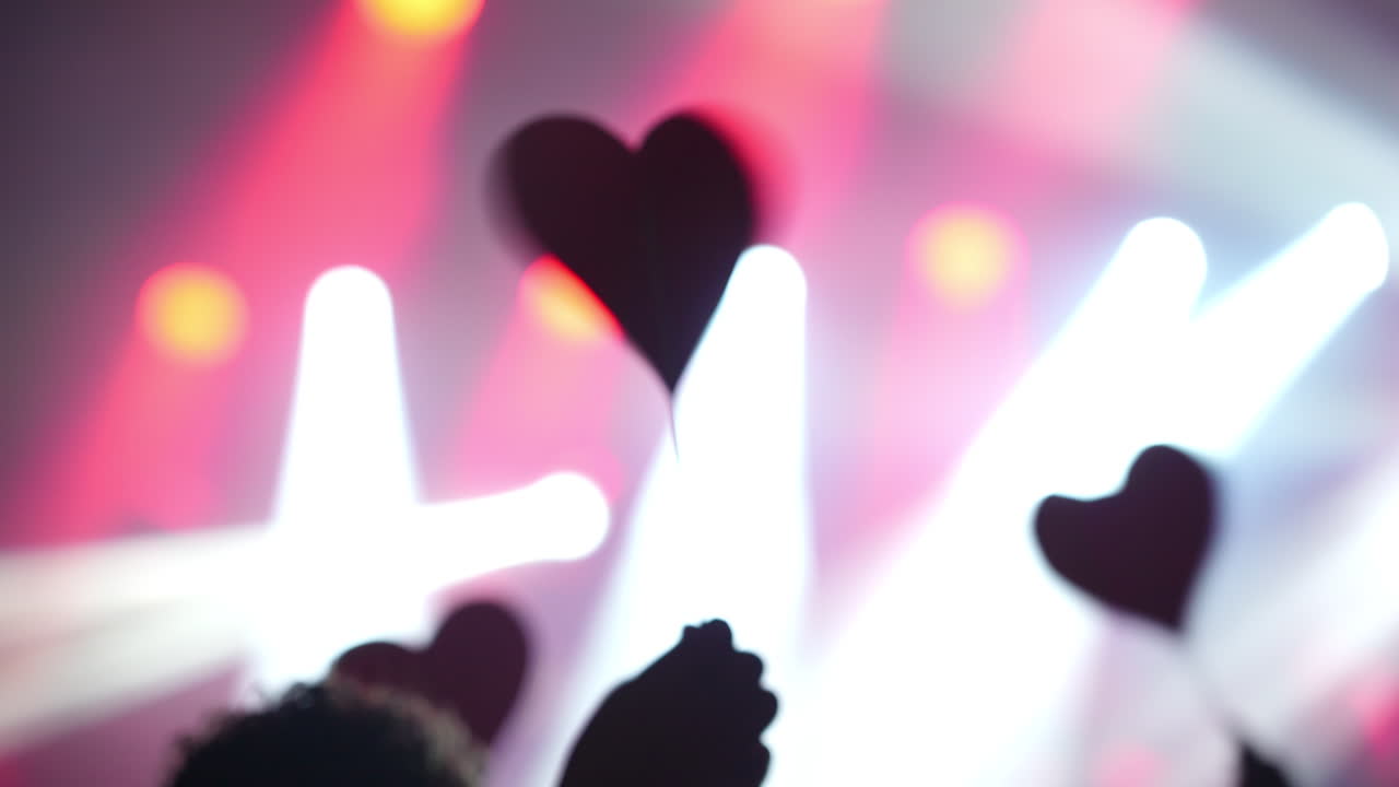 Hand holding a red heart symbol against vibrant concert lights creating a romantic atmosphere