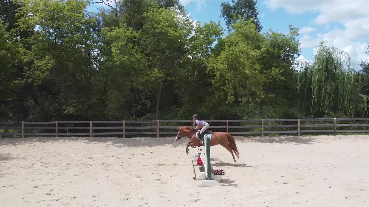 Una ragazza su un pony salta un ostacolo in un'arena equestre all'aperto in una giornata estiva.