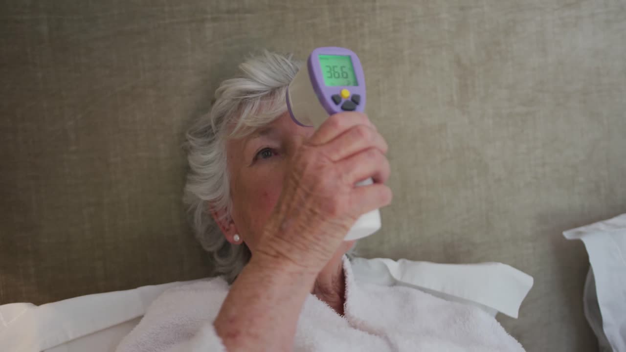Donna anziana caucasica che misura la temperatura con un termometro digitale che mostra 36,6 gradi.
