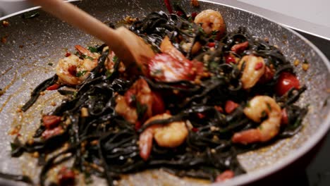 close up view of pasta been prepared with black macaroni, shrimps, coctail tomatoes and herbs over induction oven in the kitchen