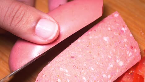 slicing pink sausage on a wooden cutting board