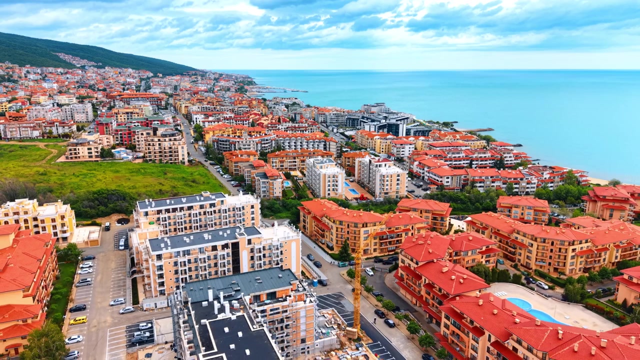 Vista aerea panoramica di una località balneare e di un cantiere. Panorama dall'alto di una città di mare con hotel dai tetti rossi, complessi residenziali e una gru da cantiere in attività.