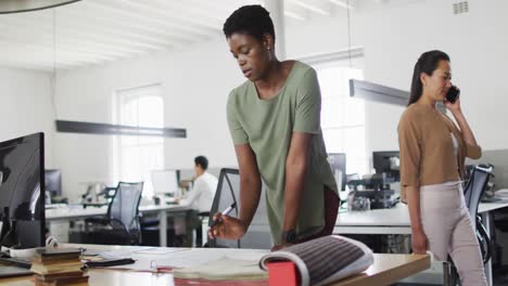 Focused-african-american-businesswoman-standing-at-desk-and-making-notes-in-office