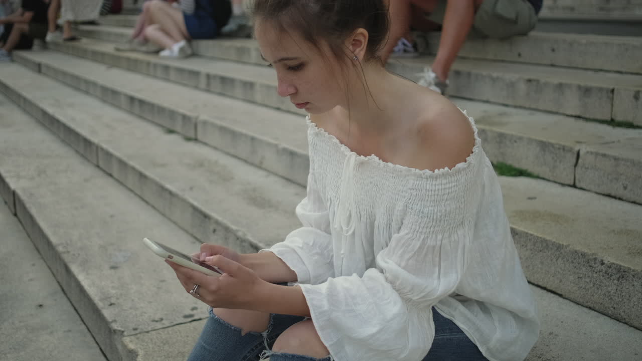 밖의 계단에서 스마트폰을 사용하는 젊은 여성