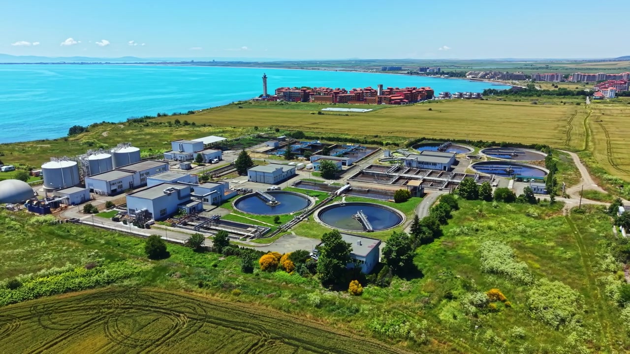 Water treatment facility near the coast with tanks and structures surrounded by green fields, showing the process of water purification near a city