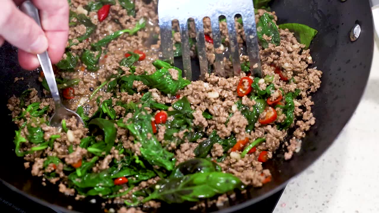 Cooking beef and basil stir-fry in a wok with vibrant ingredients under bright lighting