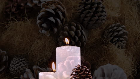 animation of lit candles and christmas decorations with pine cones in background