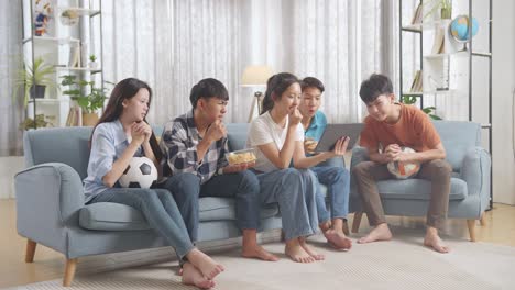 아시아 십대들이 태블릿에서 축구 경기를 응원하고 지켜보고 집에서 실망합니다.