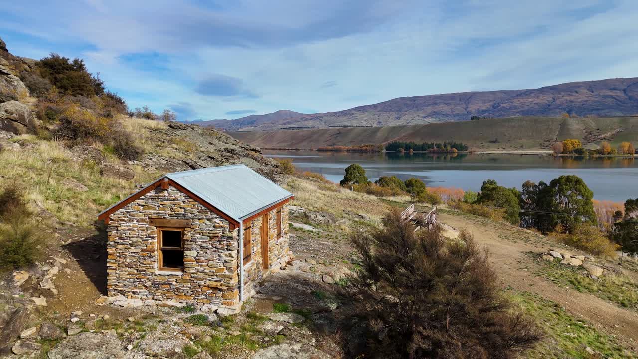 Aerial view of a rustic stone cabin near Lake Dunstan, Cromwell. Captures serene autumn landscape with clear skies and natural lighting