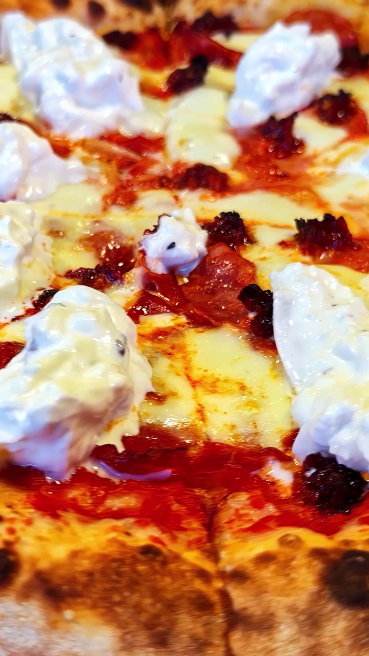 Primo piano di una pizza calda con mozzarella fusa, ciuffi di ricotta, salsa di pomodoro e crosta croccante, che mostra la sua ricca consistenza e l'aspetto appetitoso. Video verticale