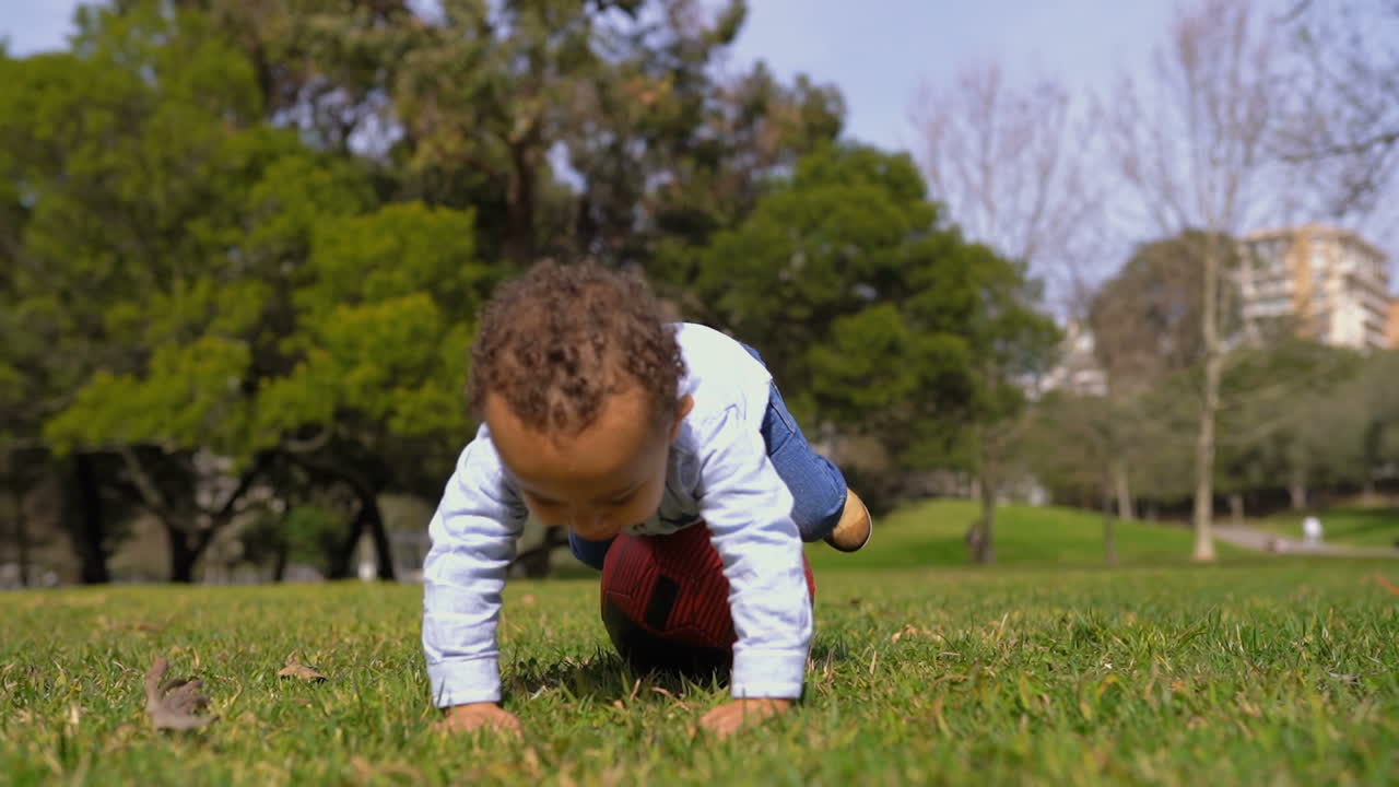 un niño de raza mixta jugando con una pelota roja en el césped en el parque