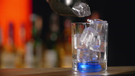 pouring ice cubes into a cocktail glass