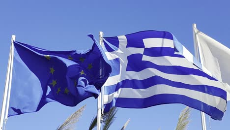 eu and greek flags flying in the wind against a clear blue sky on the isle of crete