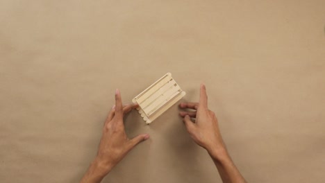 hands arranging popsicle sticks on brown surface in simple craft project, top-down view