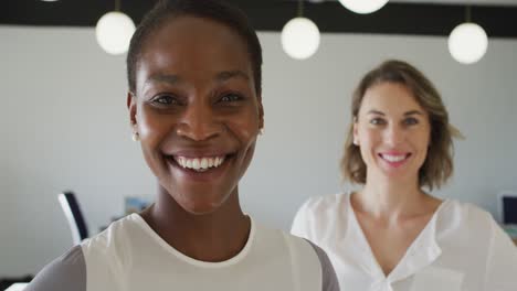 portrait of two diverse female colleagues standing and smiling in office