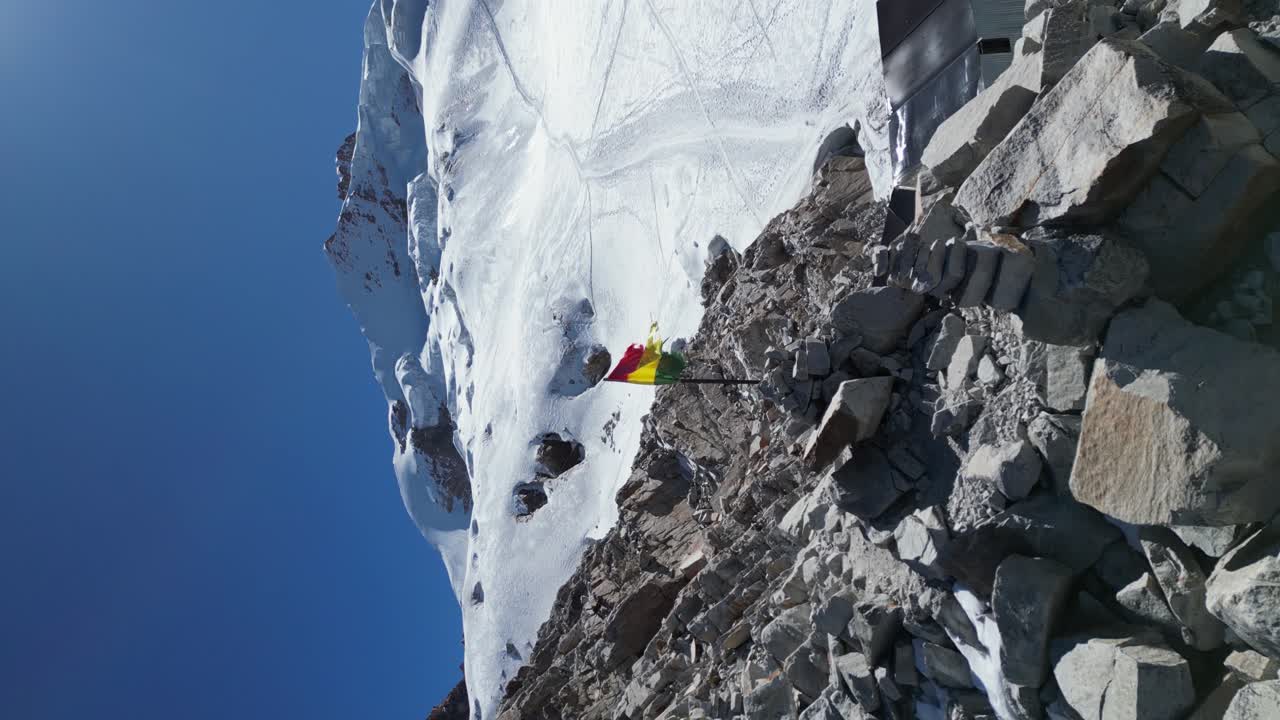 Vertical format aerial orbits Bolivia flag on rocky mountain summit