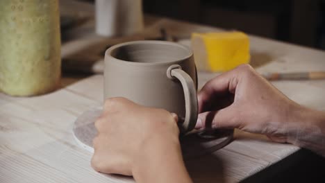 young woman attaching a small piece of clay to an edge of the handle and a cup