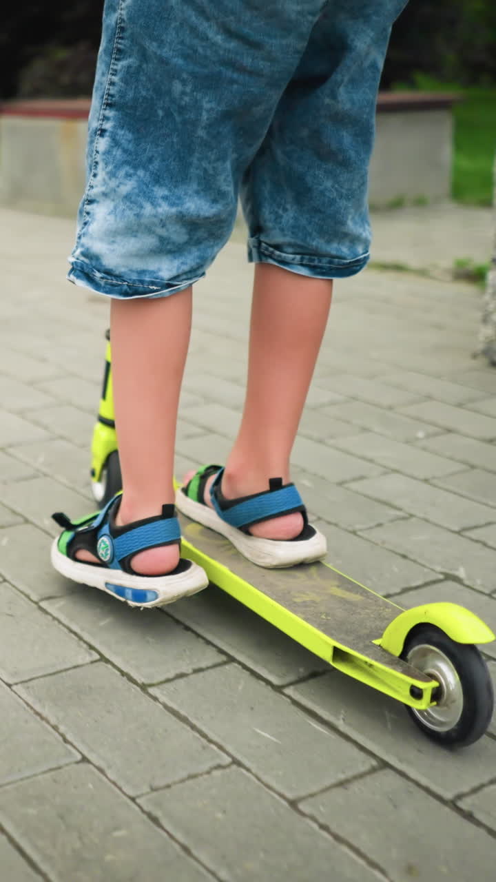 Back view of a child riding a neon yellow scooter along a smooth interlocked pathway