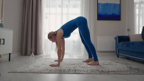 una mujer joven está practicando yoga en casa relajándose en una posición corporal simple sentada en el suelo con hermosos muebles a su alrededor. una mujer delgada con ropa deportiva de pie de rodillas inclinada hacia atrás y haciendo una postura de camello