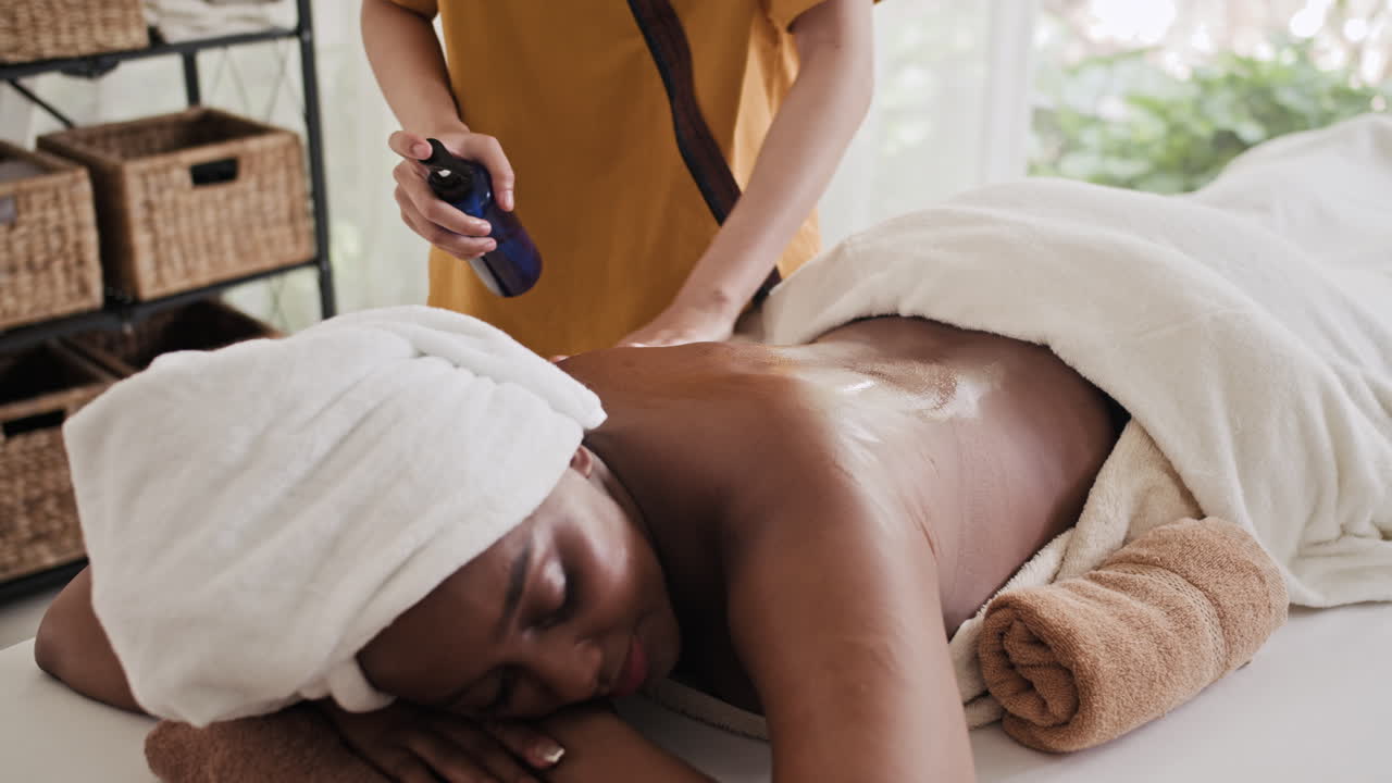 Massaggiatrice irriconoscibile che applica la crema sulla schiena di una donna in un salone
