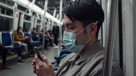 urban commuter wearing protective face mask scrolling smartphone while sitting inside subway train, capturing pandemic era daily routine and digital connectivity