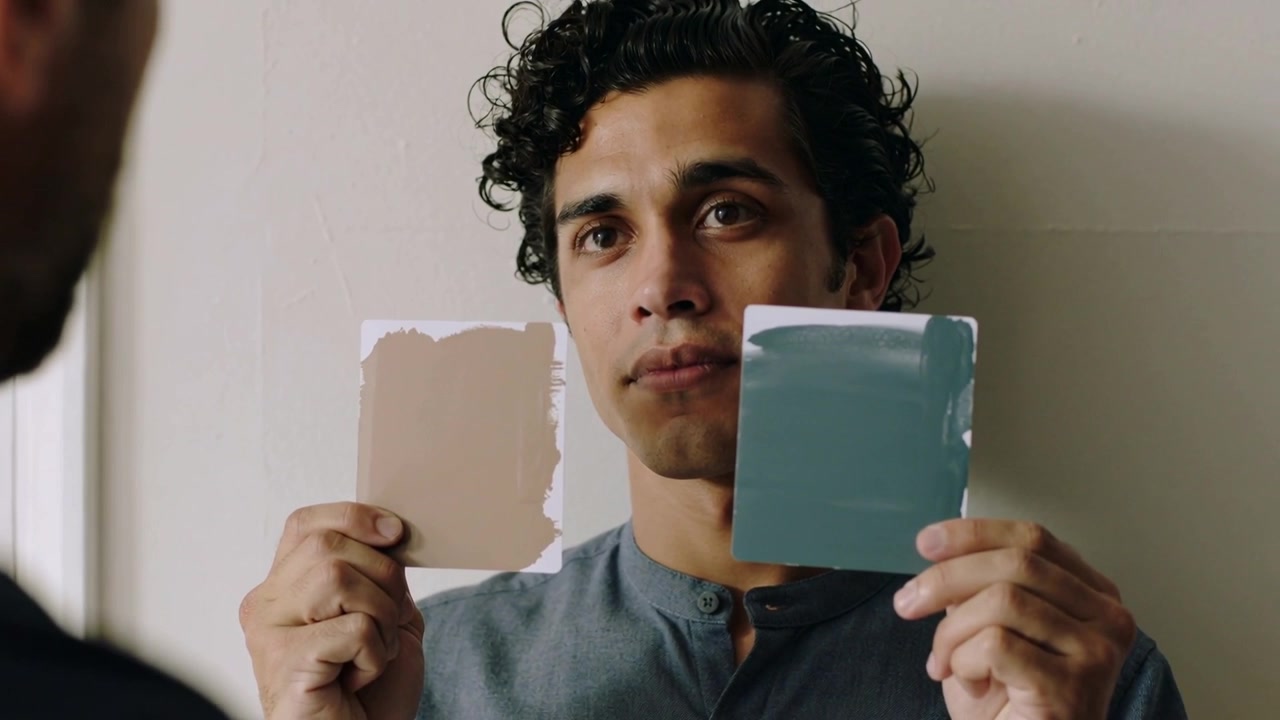 Opening eyes, man in blue-gray shirt aligning beige or teal cards on off-white wall seeking feedback
