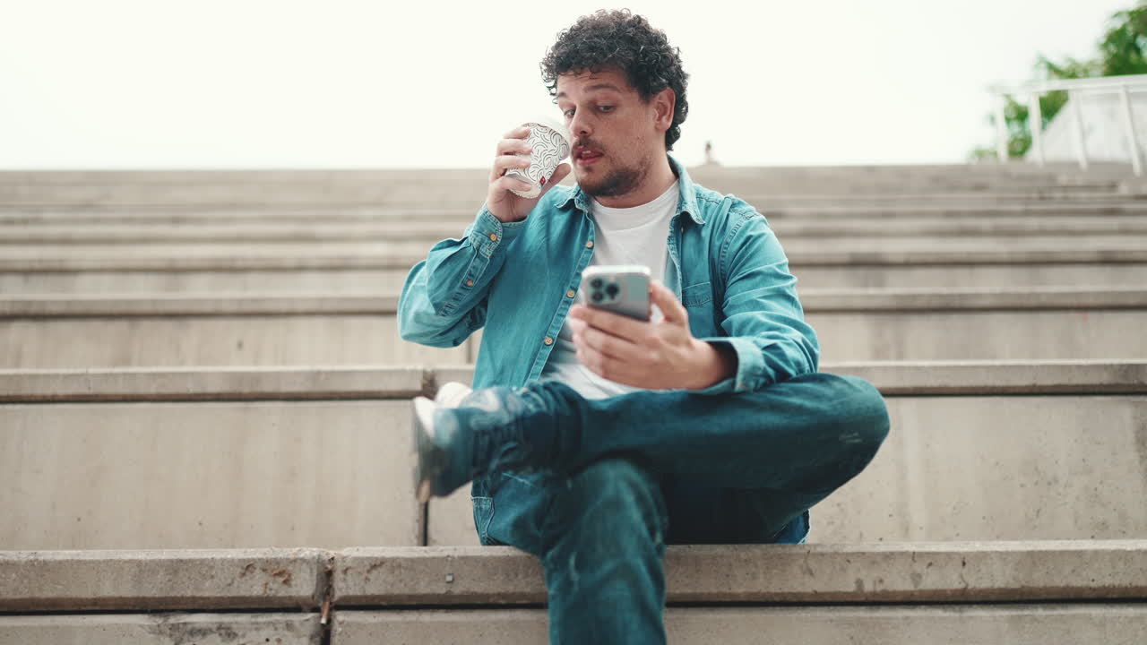 Man sitting on stairs drinking coffee and using phone