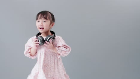 cute asian girl with headphones enjoys music and dancing, turning around happily in the studio