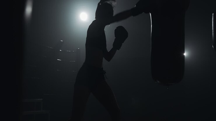 Silhouette di una pugilessa che si allena con un sacco da boxe