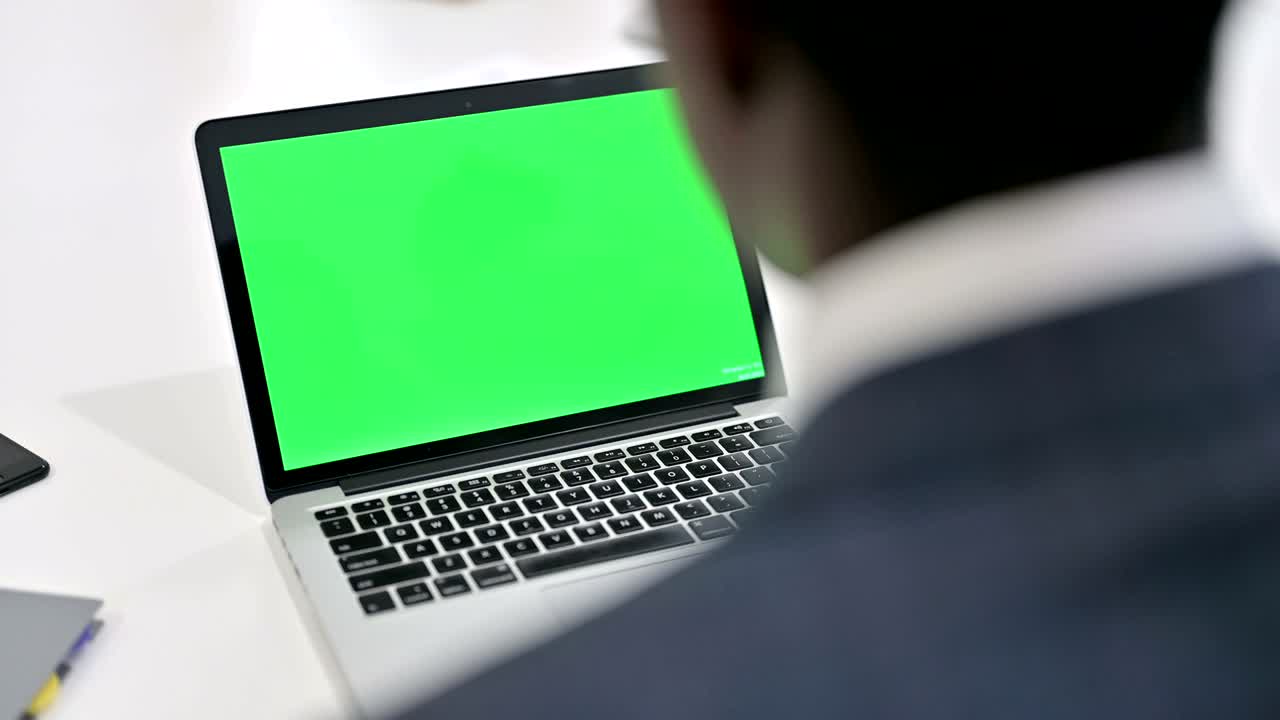 vista traseira de um empresário africano olhando para um laptop com tela de chave chroma