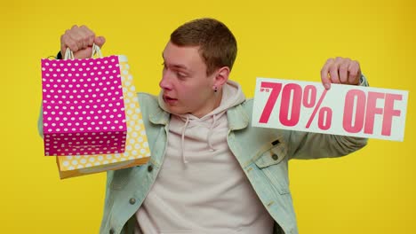 cheerful teen man showing shopping bags and up to 70 percent off inscriptions banner, black friday