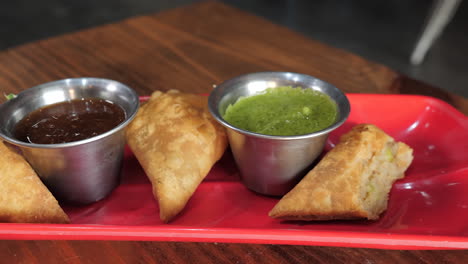 In-Koriander-Chutney-Getauchte-Samosas,-Serviert-Mit-Tamarinden-Chutney-Auf-Rotem-Teller,-Slider-Zeitlupe,-Nahaufnahme-Hd