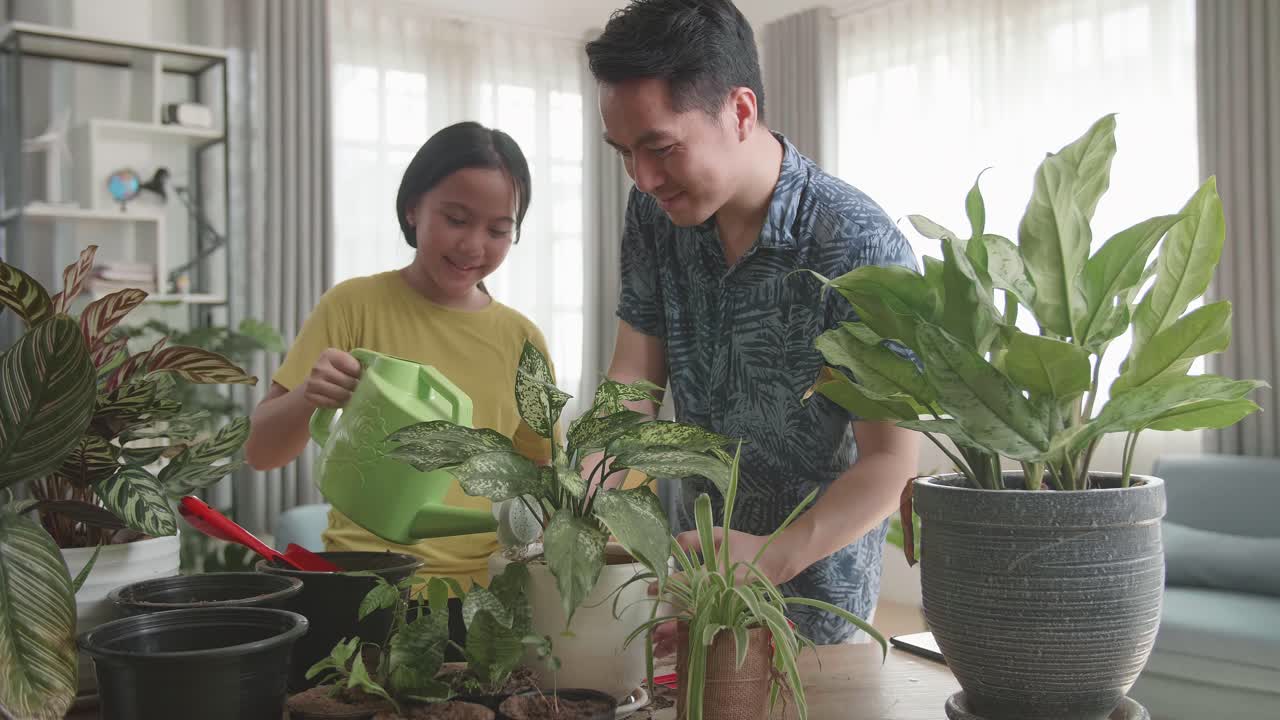 Father And Daughter Watering Home Plants At Wooden Table Indoors