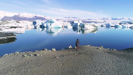 antena de una mujer parada a lo largo de la orilla de una laguna glaciar en el ártico en la laguna glaciar jokulsarlon islandia 1