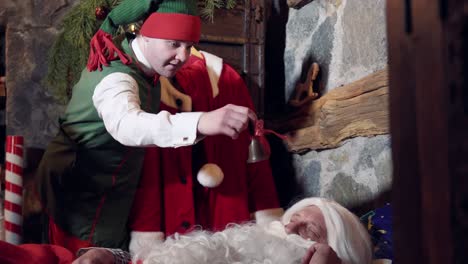 santa with white beard sleeping in his residence. funny elves ringing with a little bell to wake up santa. christmas time