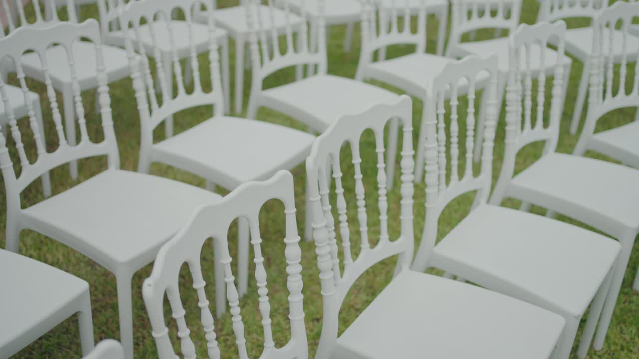 White ceremony chairs arranged in rows on grass outdoors