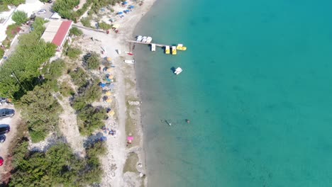 Drohnenansicht-In-Griechenland,-Die-An-Einem-Sonnigen-Tag-Auf-Kreta-über-Einen-Hell--Und-Dunkelblauen-See-Mit-Kleinen-Booten-Fliegt-Und-Von-Grüner-Landschaft-Umgeben-Ist