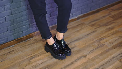 model's feet walk in massive black lacquered shoes by the wooden floor. fashionable stylish black footwear demonstration.