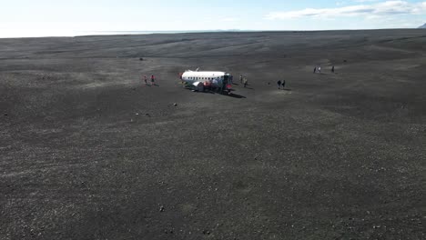 Menschen,-Die-Ein-Abgestürztes-Flugzeug-Am-Hinteren-Strand-Von-Island-Erkunden,-Fliegen-In-Der-Luft-Nach-Vorne