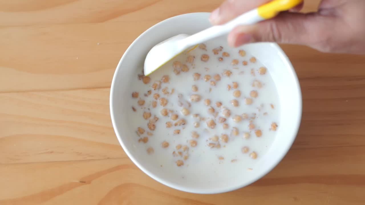 Primo piano di una mano che mescola cereali con latte in una ciotola bianca