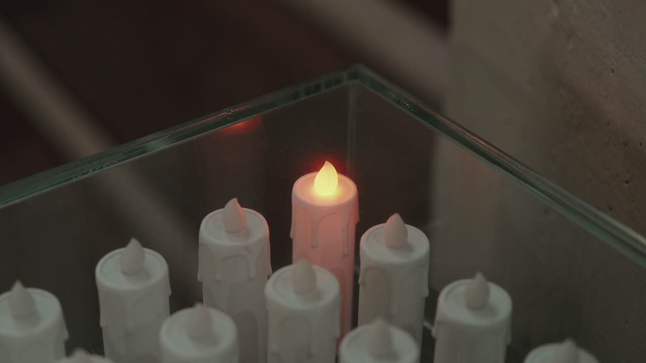 close up of a single glowing led candle surrounded by identical unlit white candles